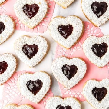 Multiple heart shaped raspberry linzer cookies with pink doilies behind.