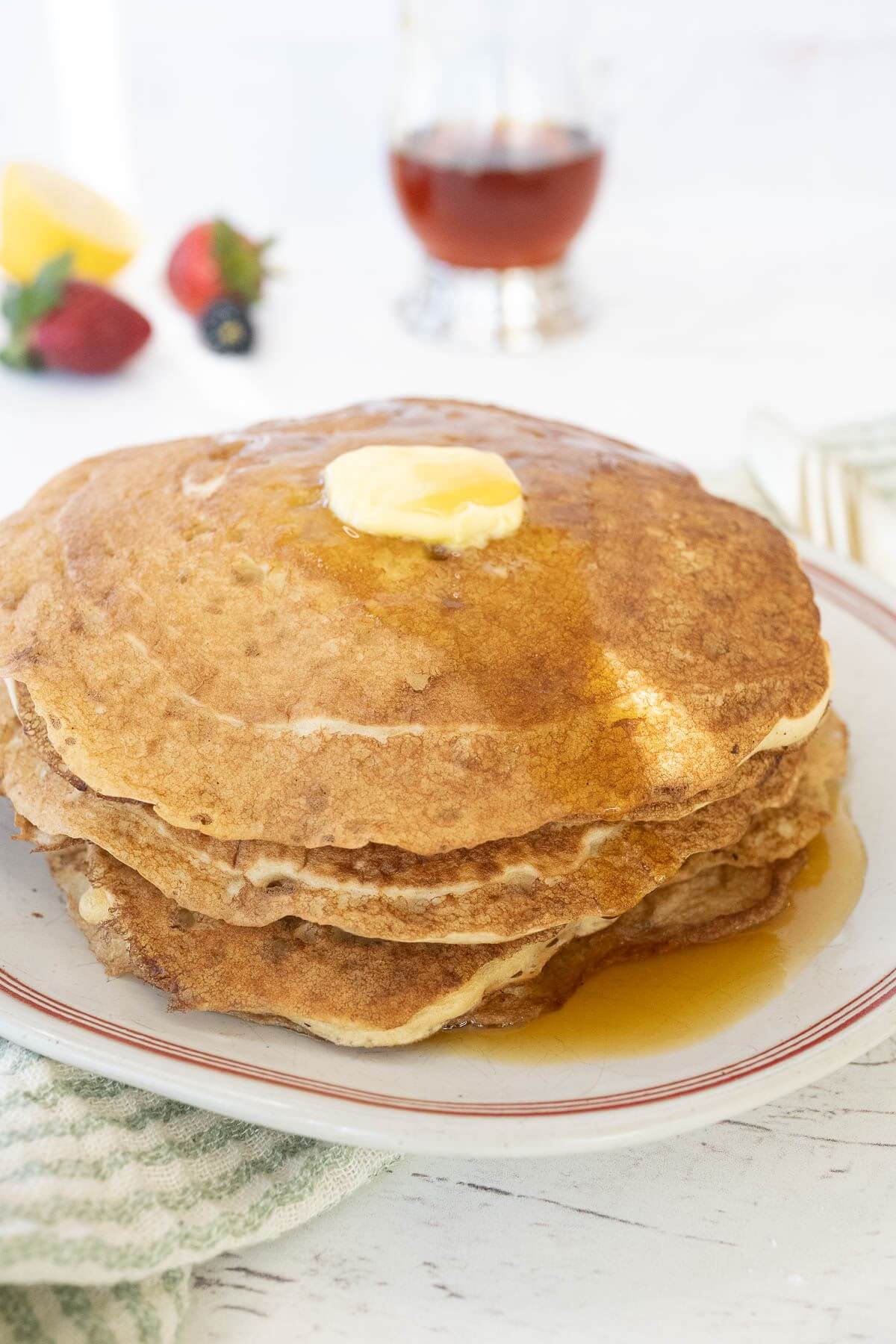 A thick stack of pancakes has a butter square melting on top.