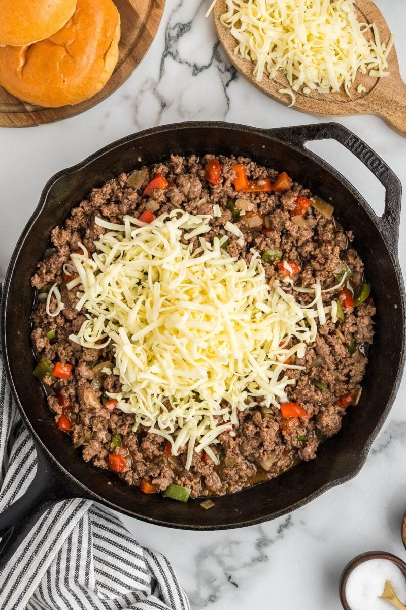 A pile of shredded cheese sits on top of the sloppy joe mixture.