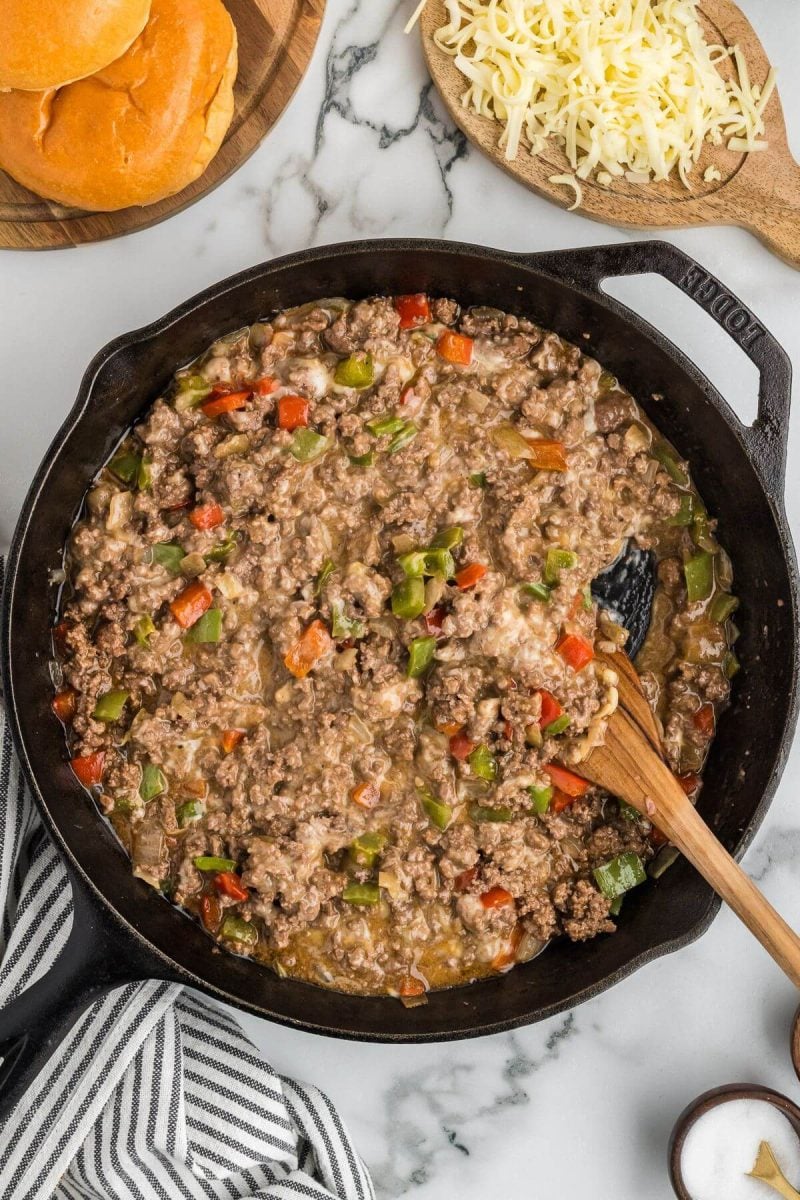 A wooden spoon stirs to melt the cheese into sloppy joe mixture. 