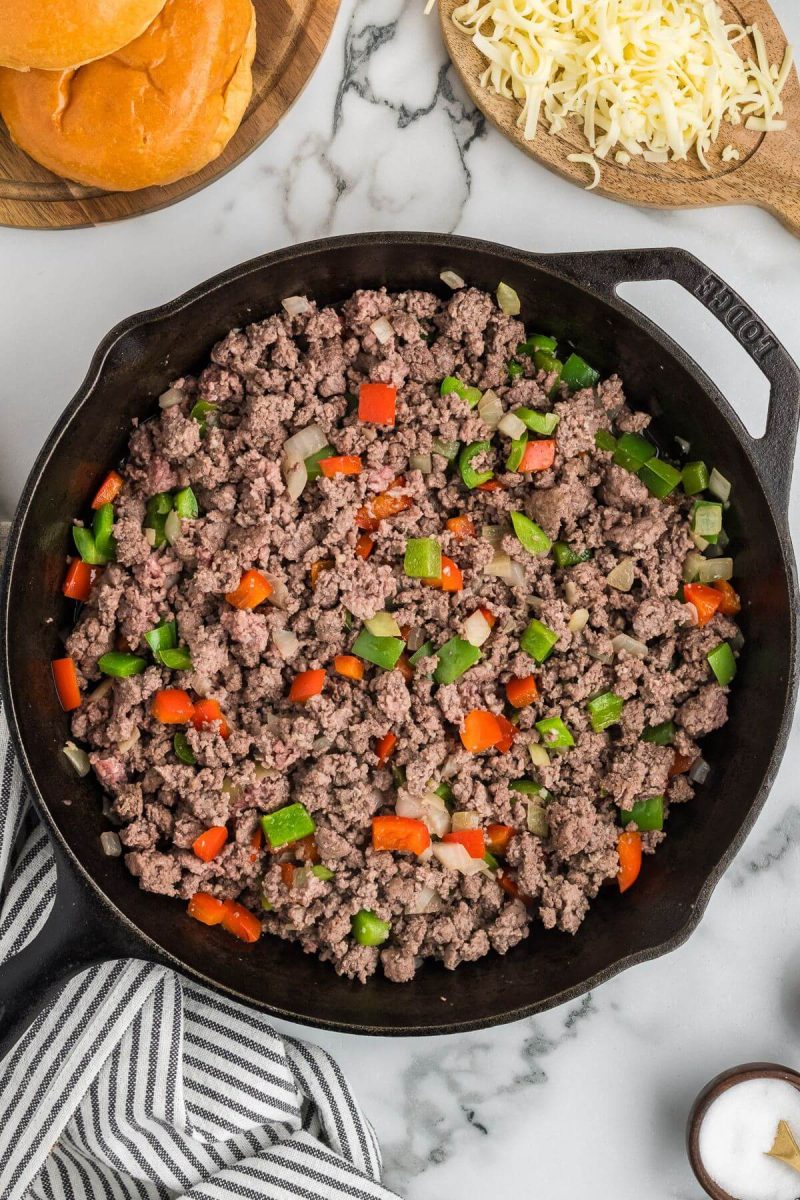 Ground beef cooks in a skillet along with peppers and onions.