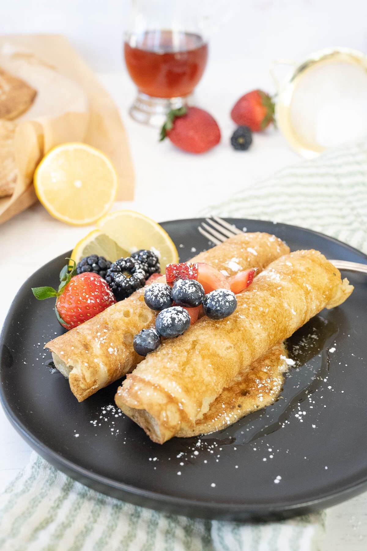 A black plate holds two rolled up pancakes with blueberries, blackberries, and strawberries.