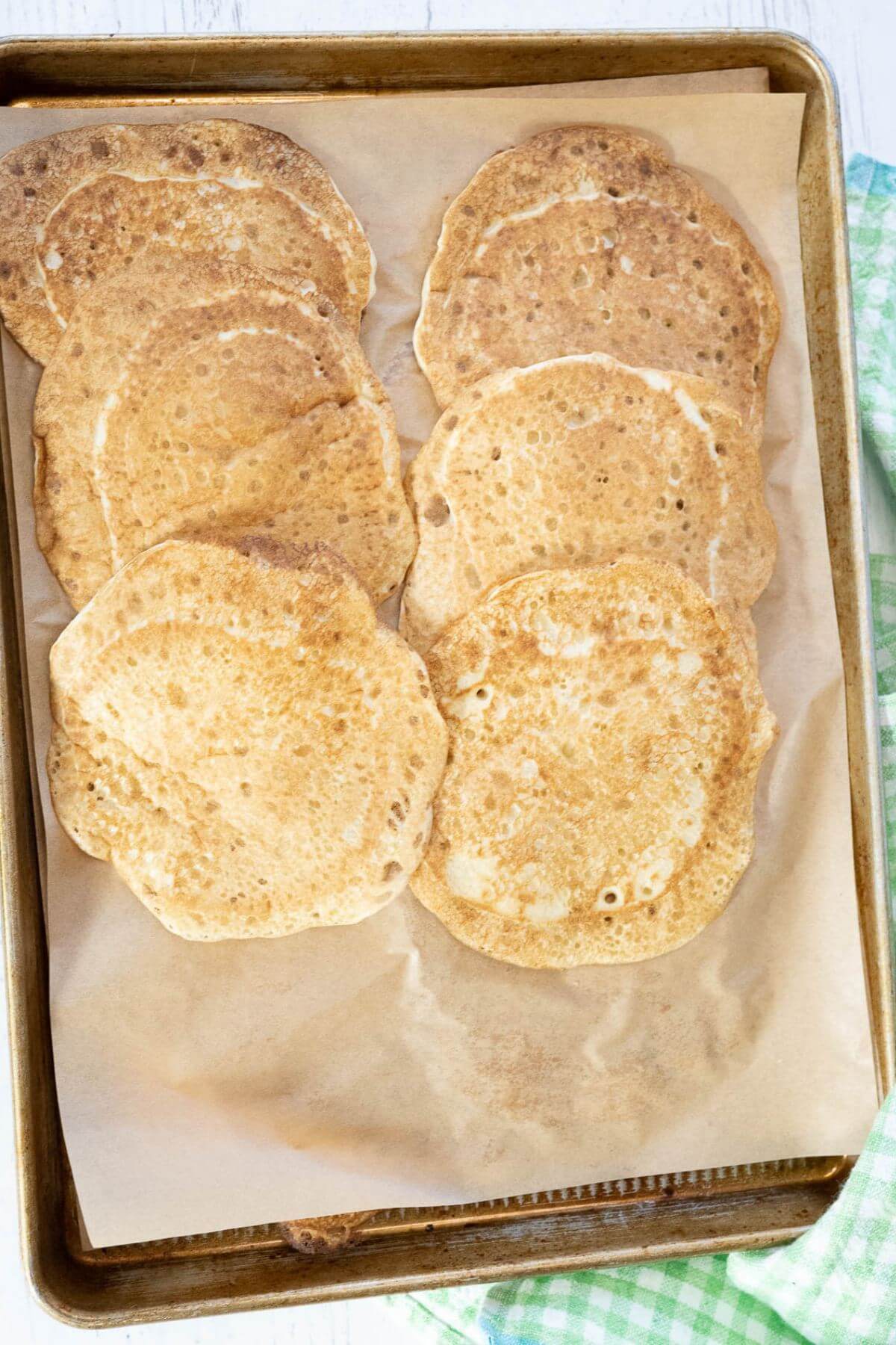 Parchment paper lined cookie sheet holds rows of pancakes with space at end of pan.