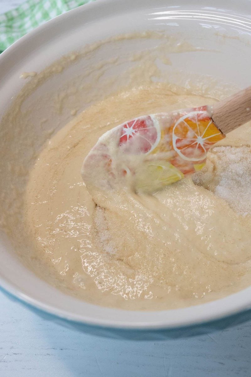 A red and orange spatula stirs sourdough starter in bowl.