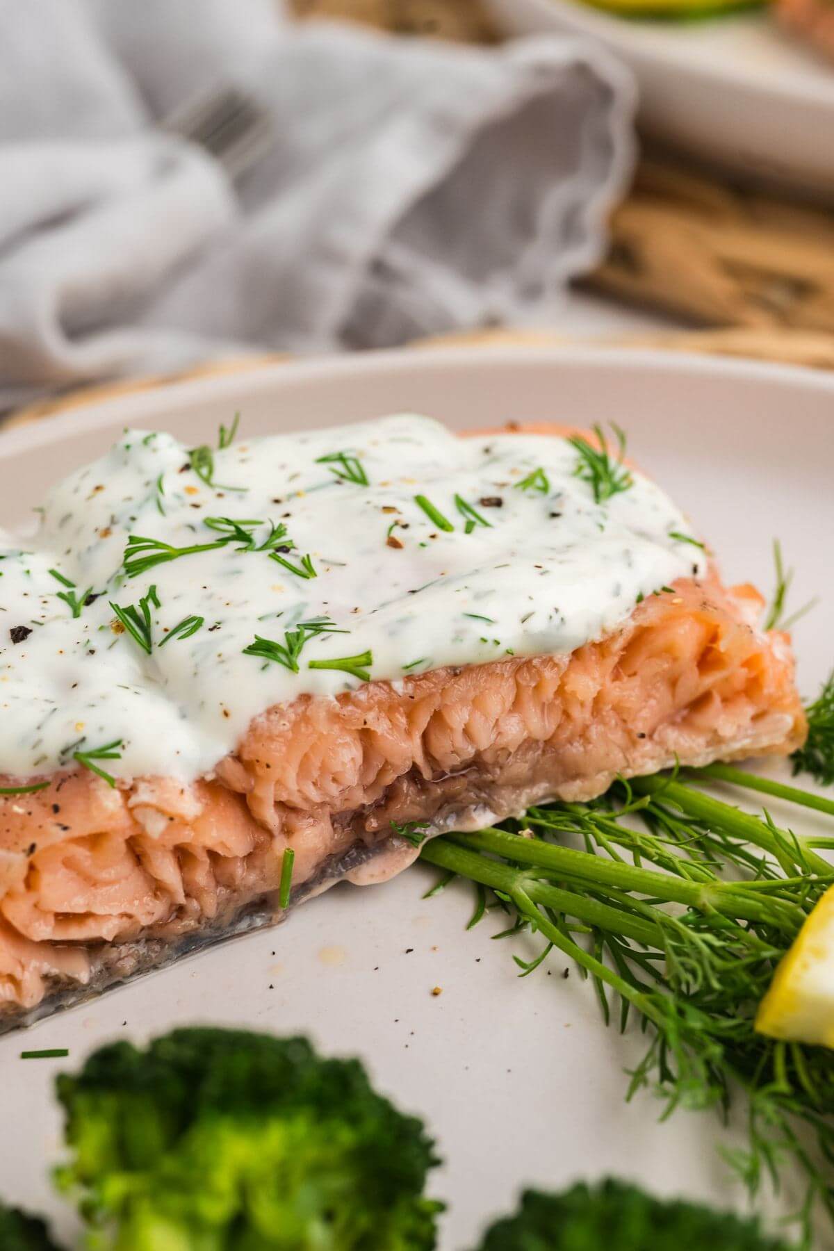 A large piece of cooked salmon is shown up close focusing on the tender inside and dill sauce on top.