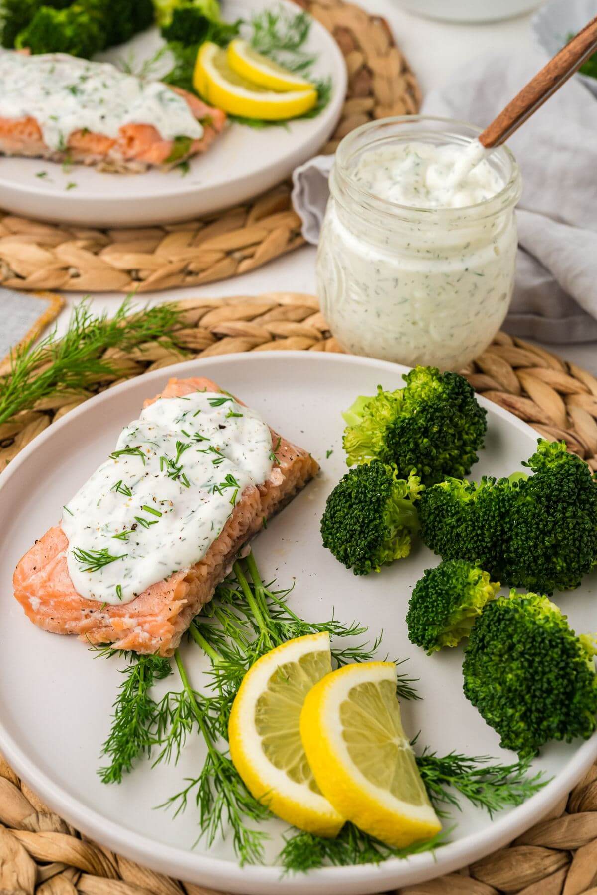 Bright green broccoli and dill contrast with bright yellow lemons and pink salmon on white plates.