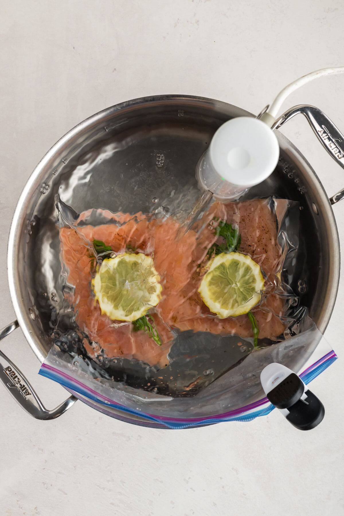 A Ziploc bag with salmon filets cooks in a water-filled pot sous vide style.