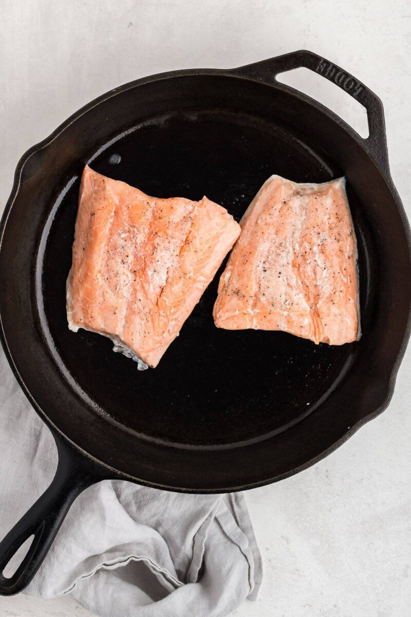 Two salmon pieces sear in an iron skillet.