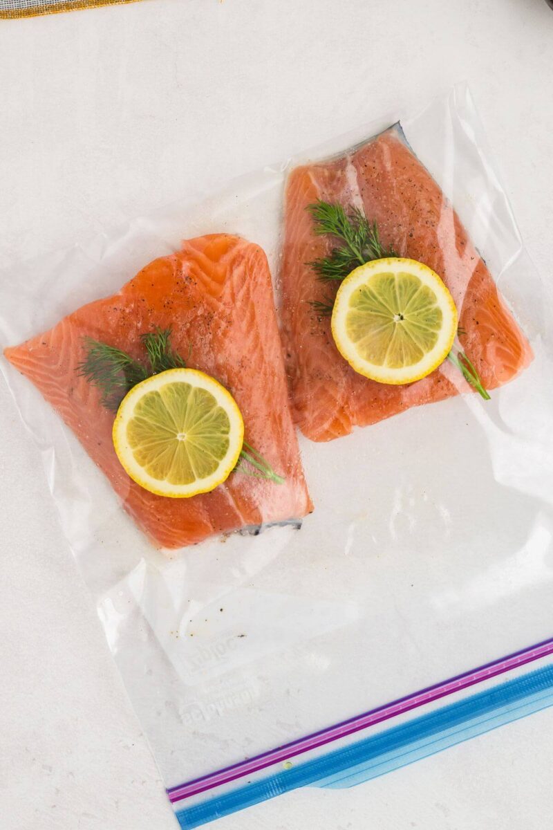 A Ziploc bag holds two filets of salmon, fresh dill, and lemon slices.