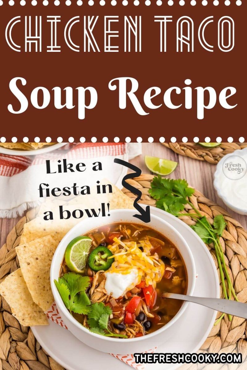 A bowl of southwestern soup topped with veggies, cheese, sour cream and more is on a braided placemat, to pin.