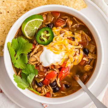 Tortilla chips are beside bowl of soup topped with veggies, cheese, and sour cream.