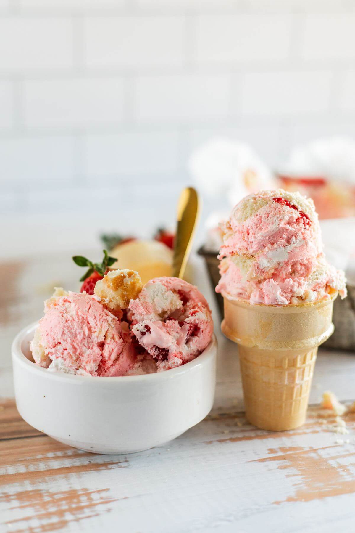 A full ice cream cone sits next to a full bowl of homemade strawberry ice cream. 
