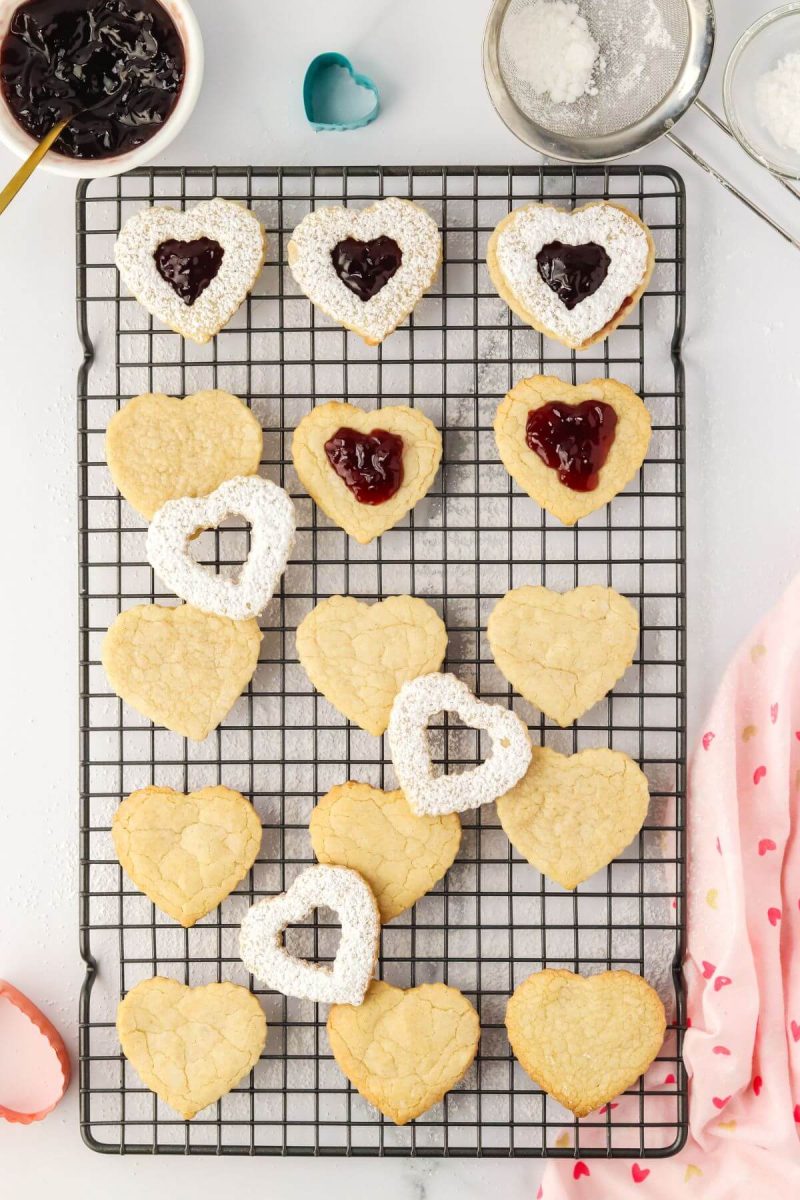 Heart shaped cookies are being put together, some have powdered sugar and jam.