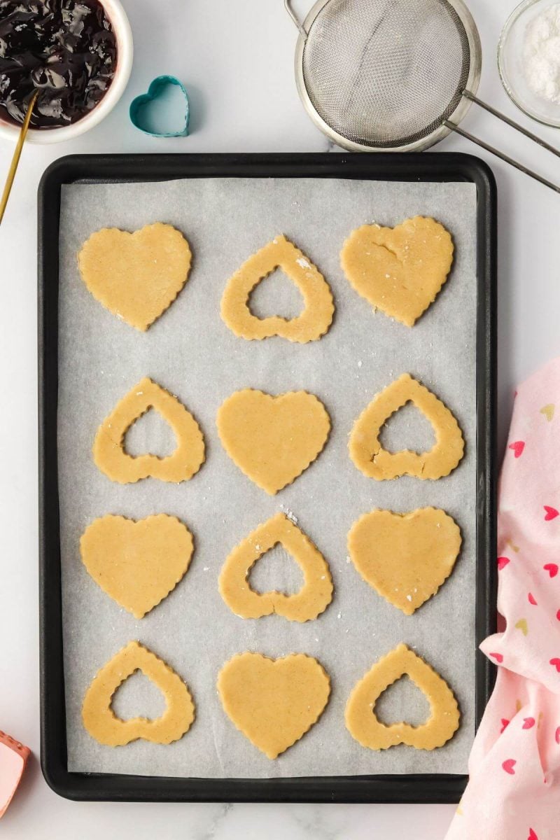 Heart shaped cookie dough with some with empty centers sit on cookie sheet.