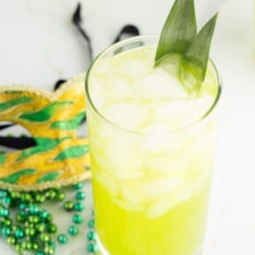 Bright neon yellow-green Hand Grenade drink with mardi gras mask and beads behind.