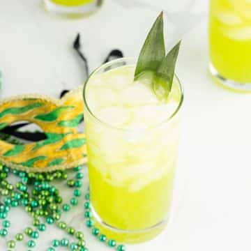 Bright neon yellow-green Hand Grenade drink with mardi gras mask and beads behind.