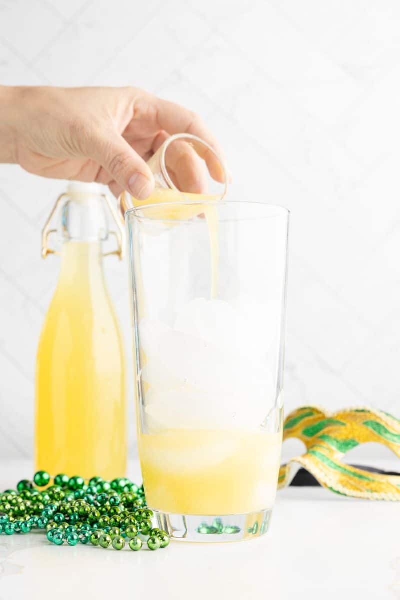 Hand pouring pineapple juice into shaker with ice. 