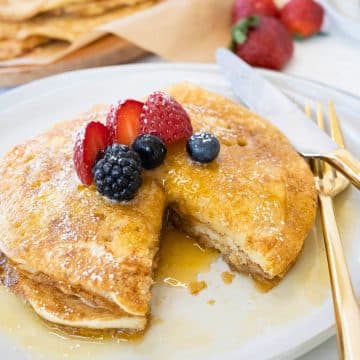 Stacked sourdough pancakes with wedge removed and berries on top.
