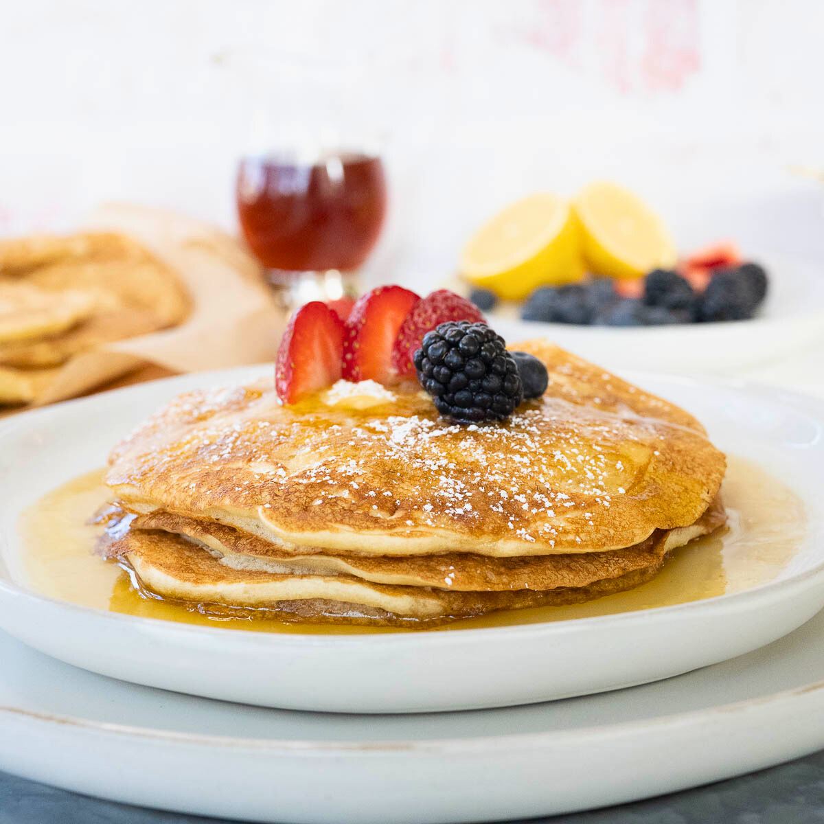 A fluffy stack of sourdough pancakes with fruit on top drizzled with maple syrup. 