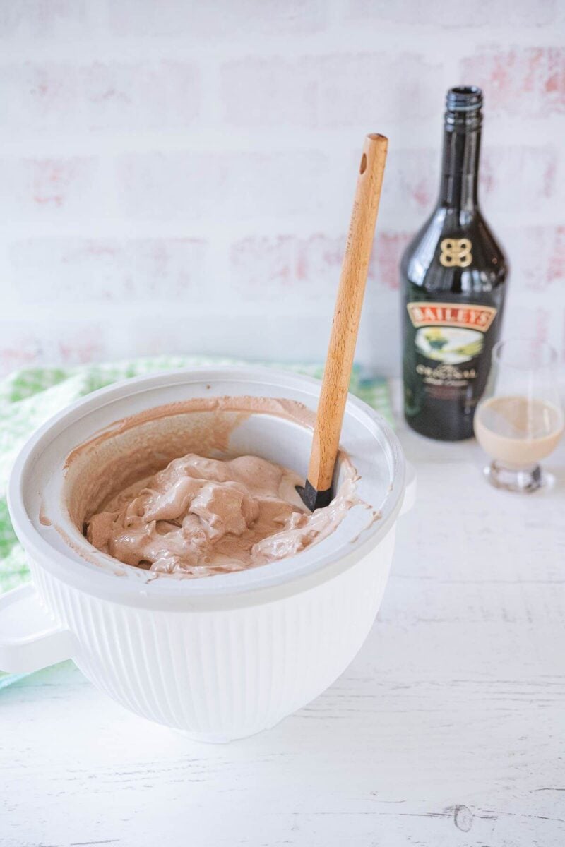 The ice cream machine bowl with soft serve sits next to glass and bottle of Baileys.