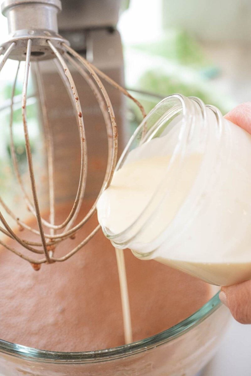 A hand pours heavy cream from jar into mixing bowl.