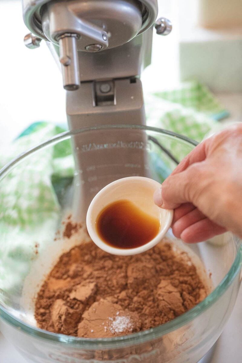 Someone's hand pours vanilla extract into mixing bowl.