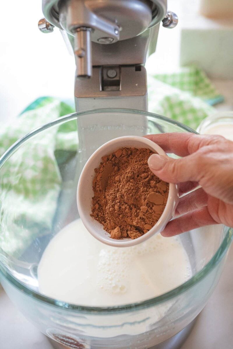 A hand pours cocoa powder into mixing bowl.