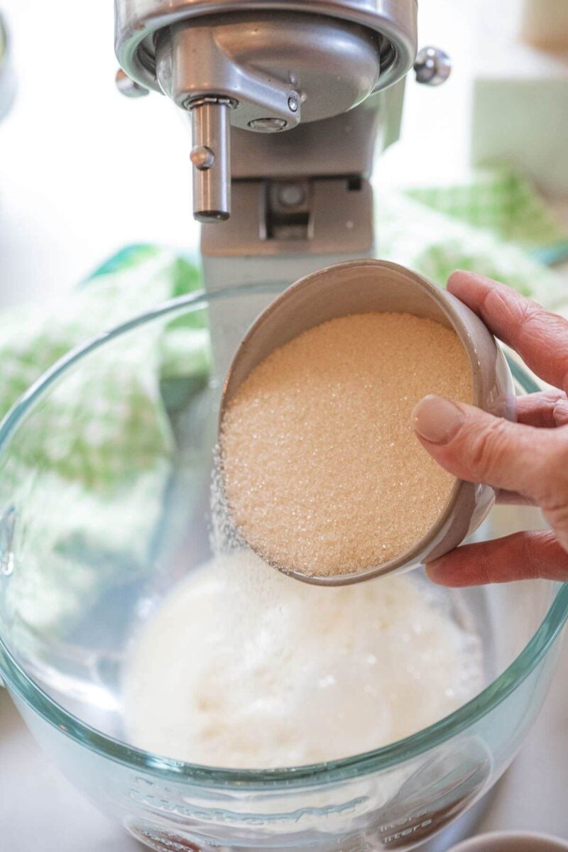 A hand pours sugar into mixing bowl.