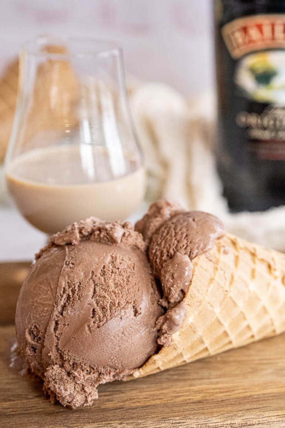 An ice cream cone is on its side in front of Baileys bottle and glass.