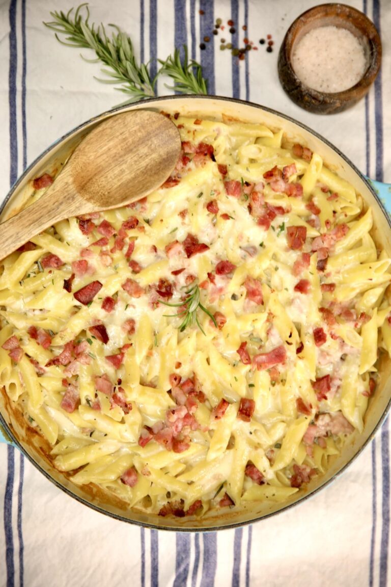 Baked ham and penne pasta in a skillet with a wooden spoon.
