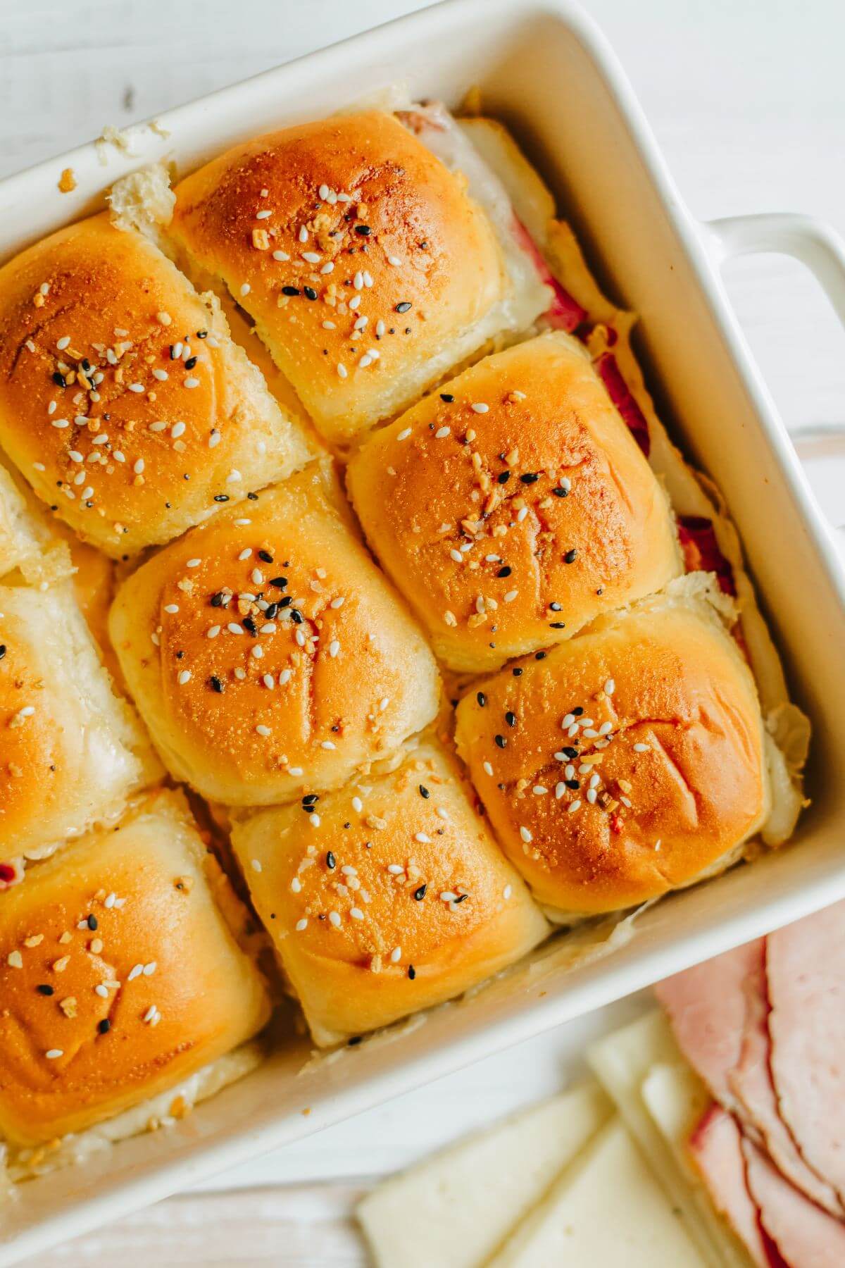 Baked sliders with seasoning on top are shown in a baking dish at an angle.
