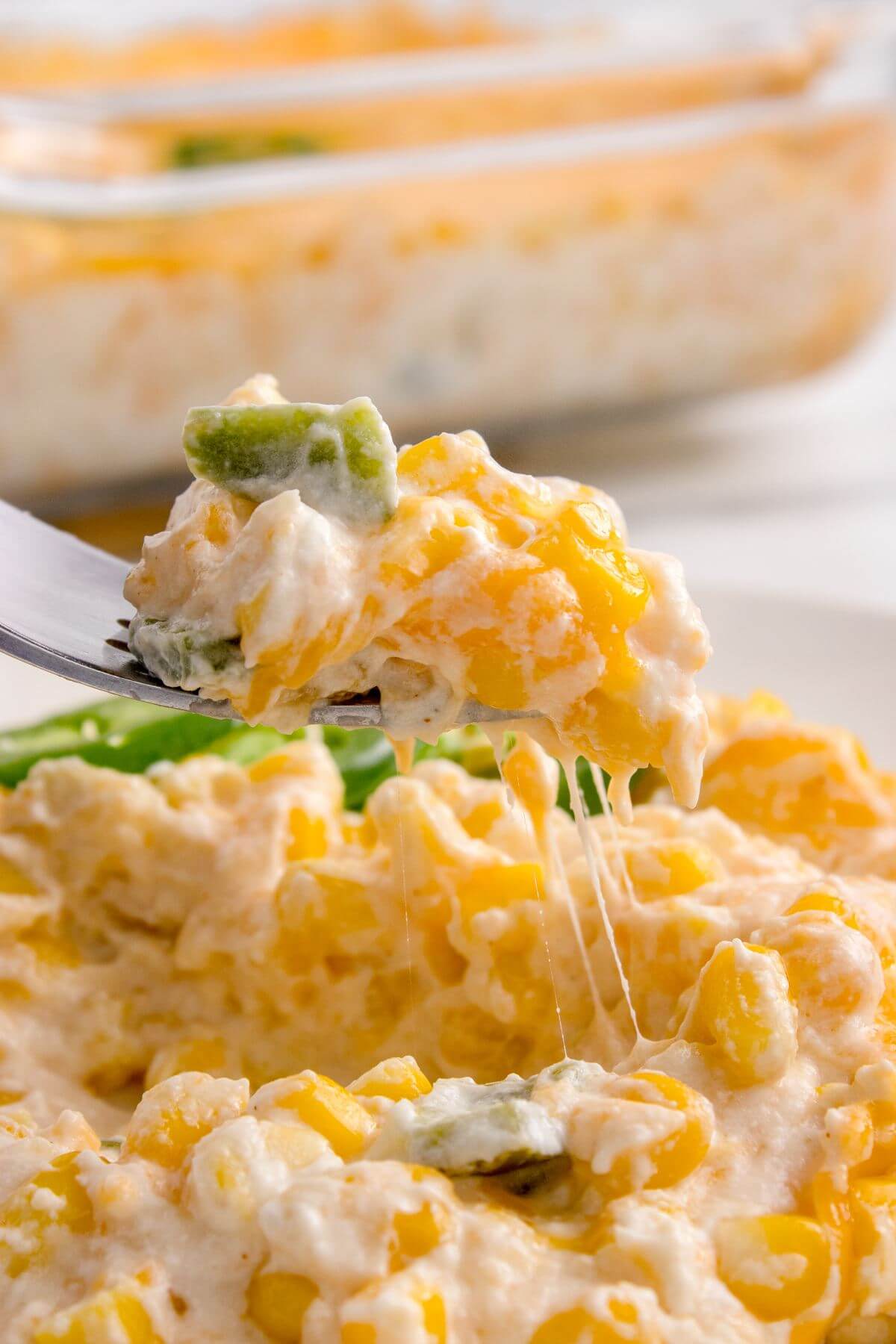 Creamy, cheesy casserole showing diced jalapenos and corn kernels is lifted by a fork.