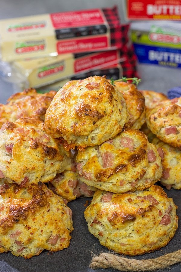 Cheesy ham biscuits stacked with white cheddar behind.