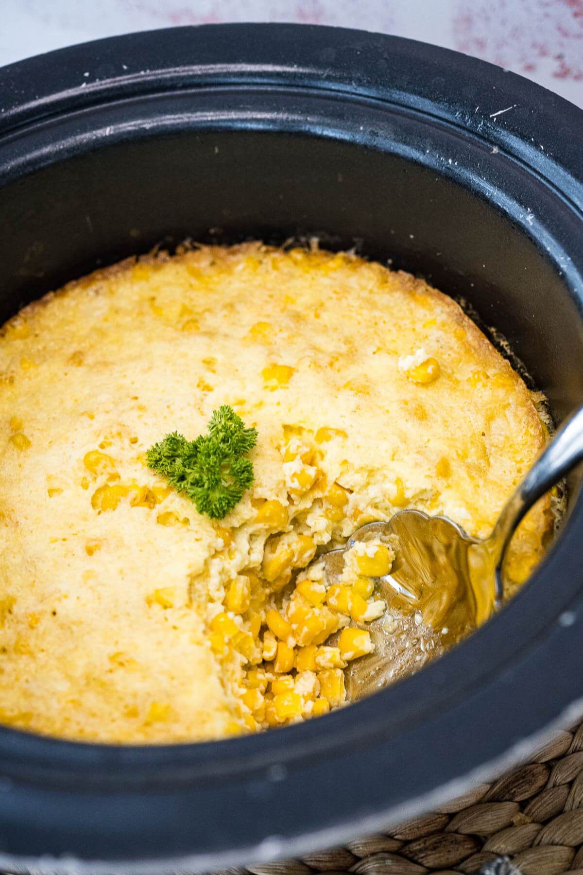 Spoon taking out serving of crock pot corn casserole. 