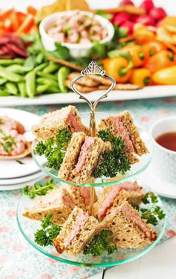 Triangles of deviled ham sandwiches on a tiered serving tray.