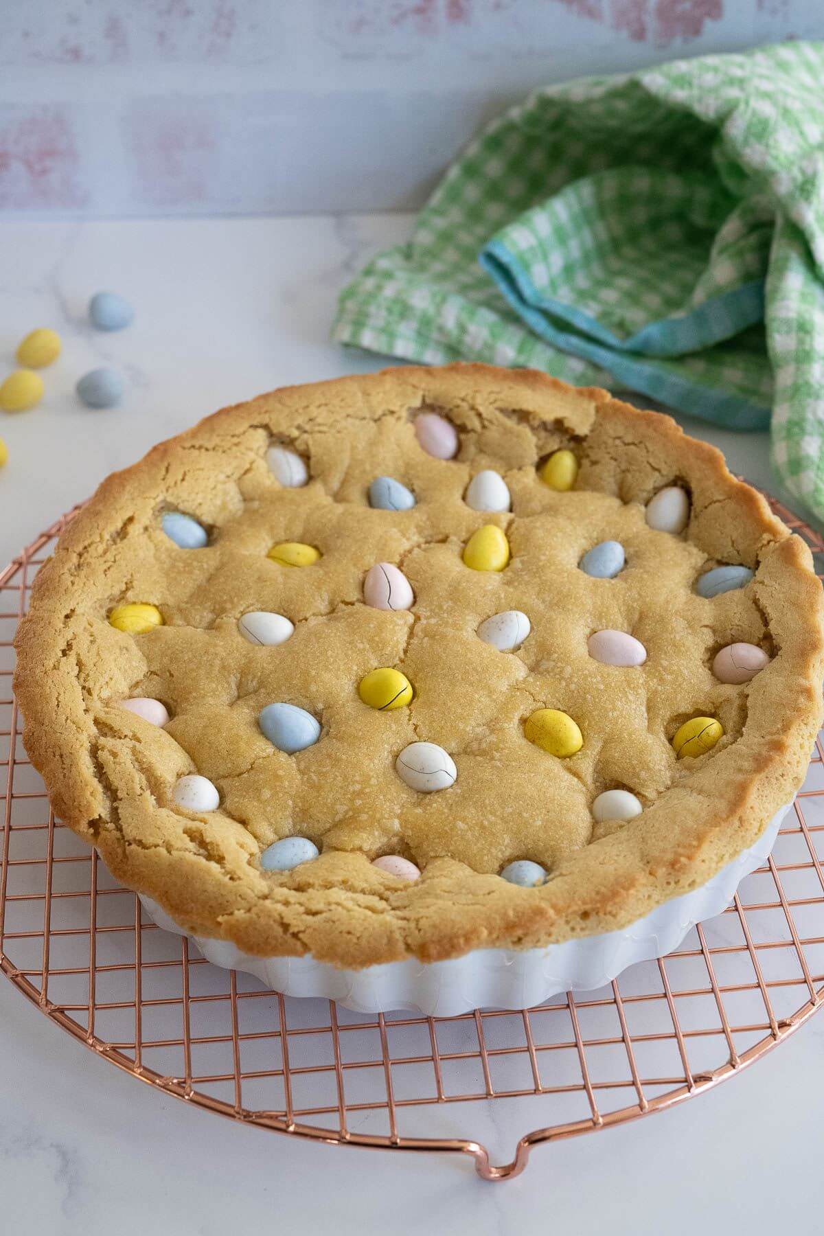 A baking dish full of giant cookie has candy eggs on top and sits on wire rack.