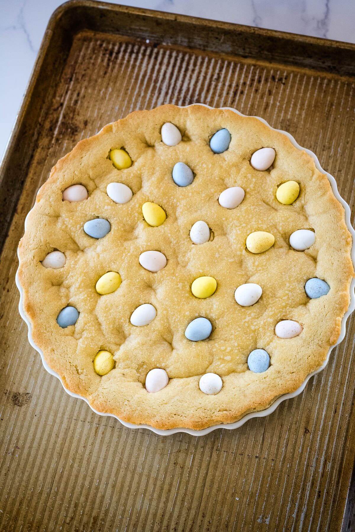 A pan of golden cookie crust with candy eggs rests on a cookie sheet.