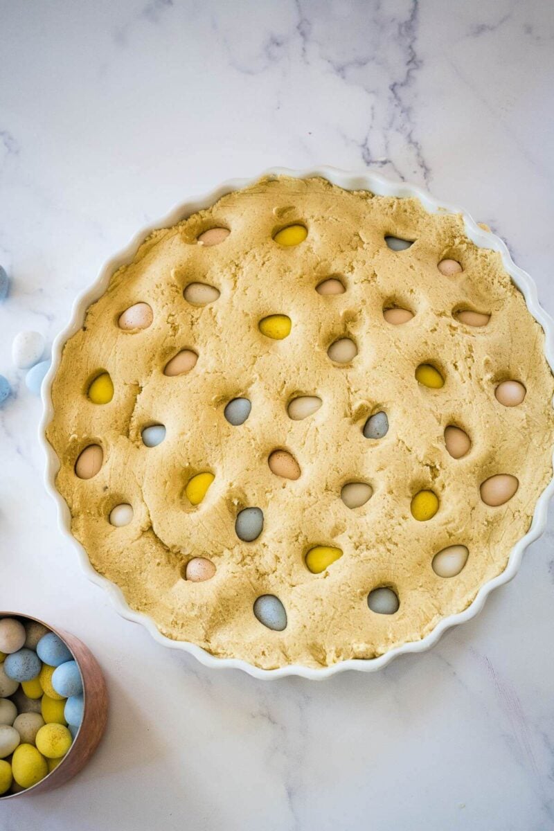 A small dish of candy eggs sits next to tart dish of cookie with candy eggs pressed into top.