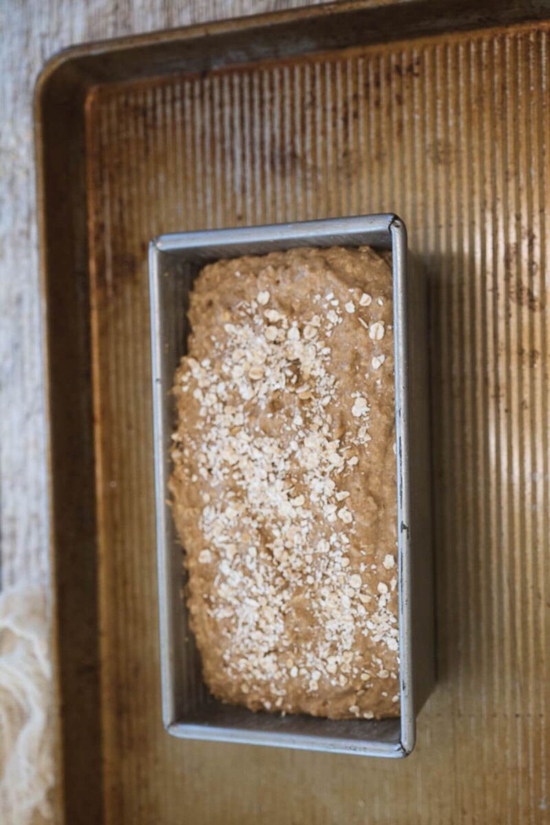 A bread pan is filled with bread batter and topped with rolled oats.