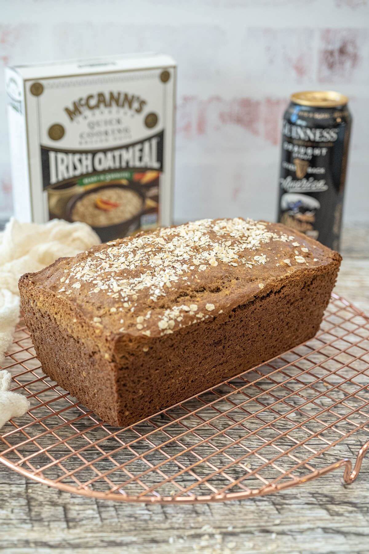 A loaf of bread rests on copper wire rack with oatmeal and Guinness beer behind it.