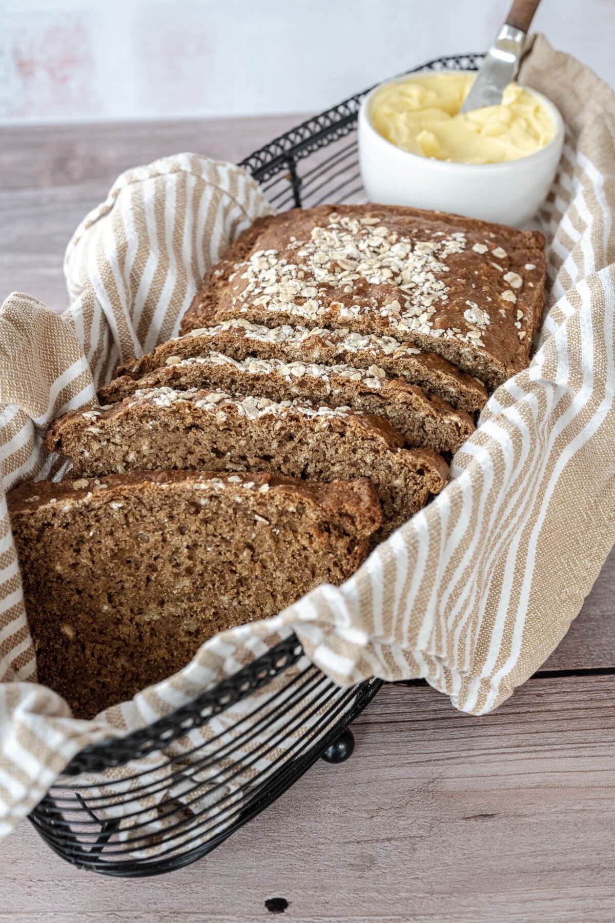 A butter dish is in a black wire basket along with slices of bread.