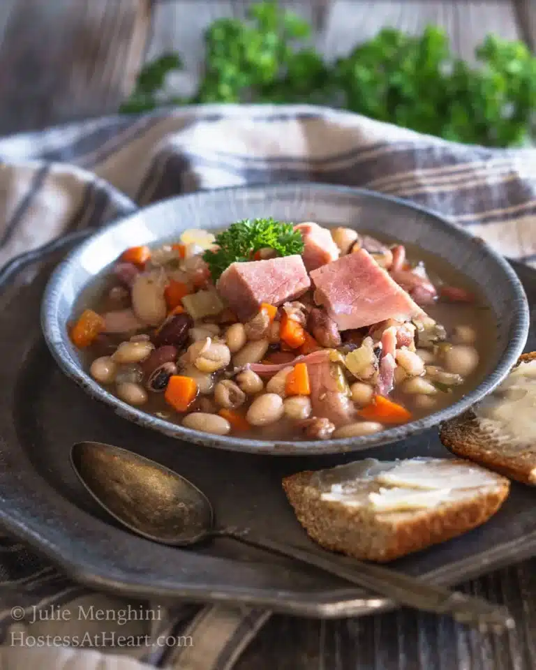 Chunky and brothy ham and bean soup in a bowl with slices of bread.