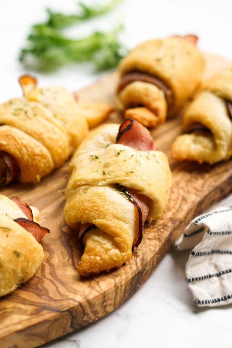 Ham and cheese crescent roll ups on a wooden serving board.