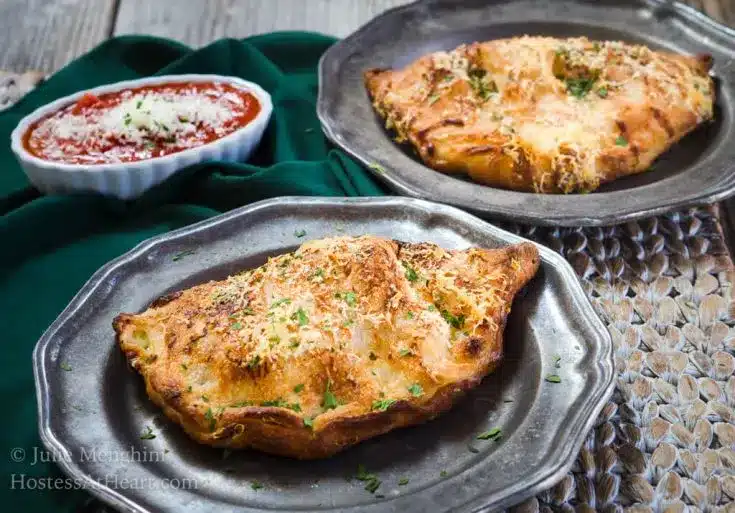 Ham and cheese calzones on plates with marinara sauce behind.