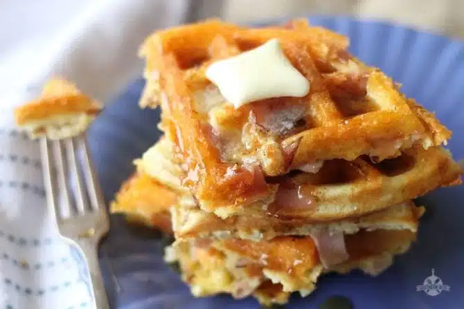 Ham and cheese waffles stacked on a plate with butter and syrup.