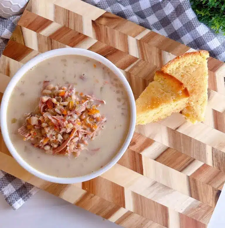 Ham and navy bean soup in a bowl on a cutting board with servings of cornbread.