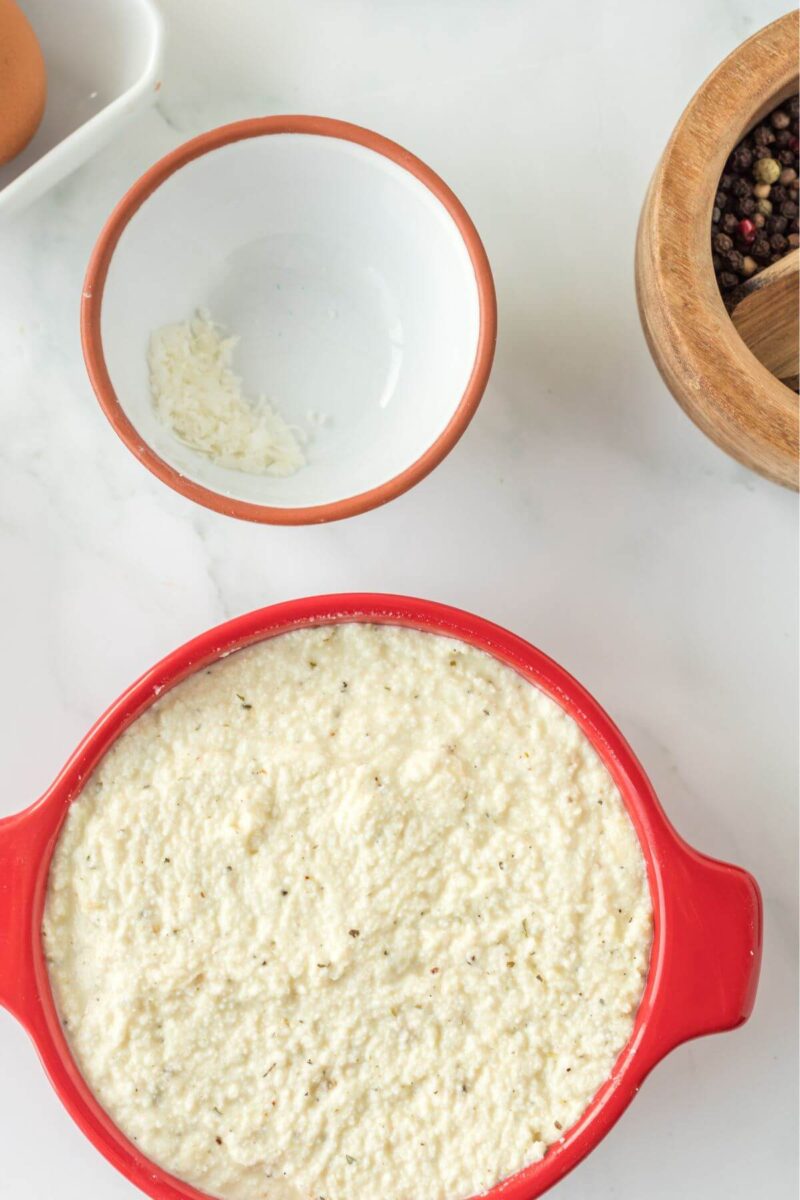 A red ramekin full of ricotta cheese mix sits next to an empty bowl.