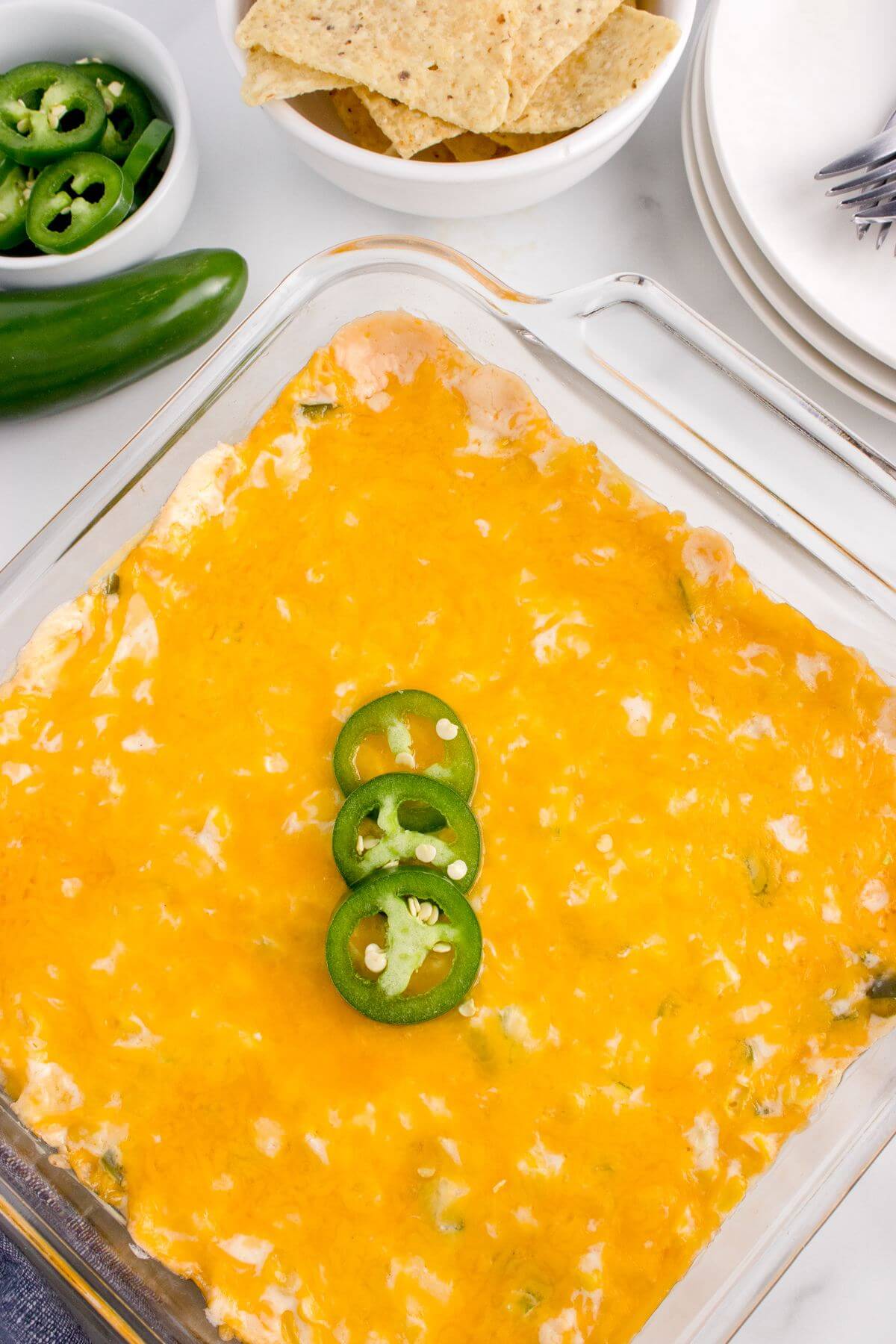 Tortilla chips and jalapenos frame a glass casserole dish covered in yellow cheese.