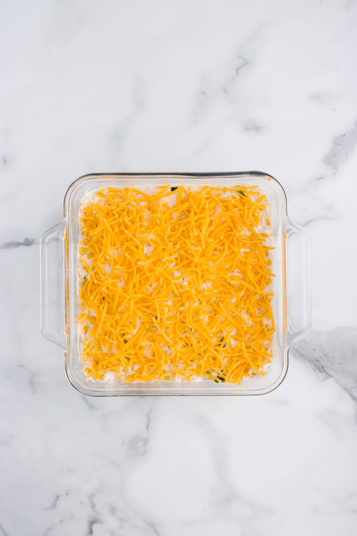 A glass square pan is topped thickly with cheddar cheese.