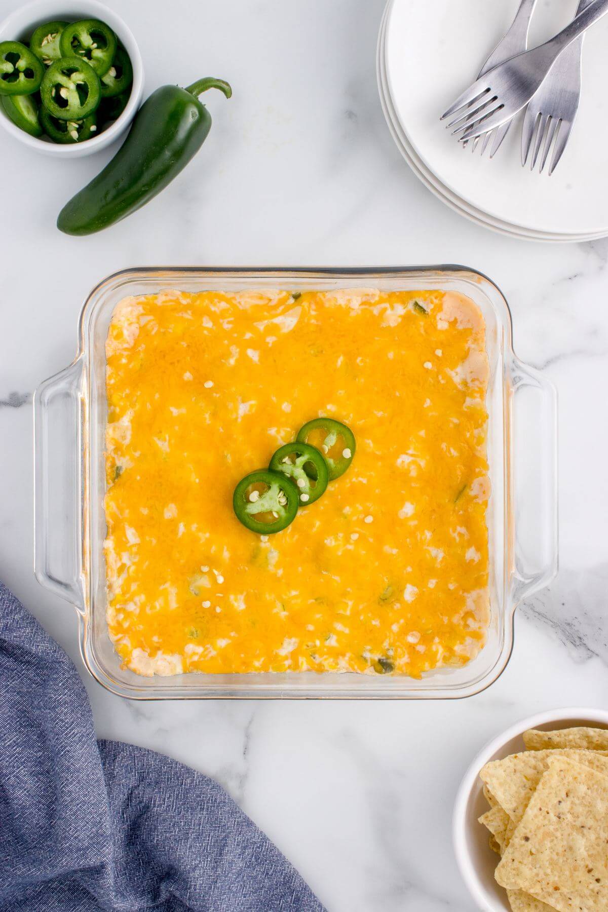 A square glass pan is filled with baked casserole garnished with jalapeno slices.